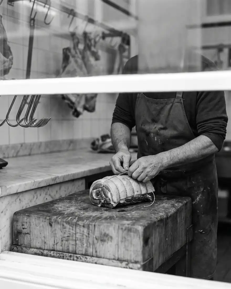 Les mains d’un boucher ficelant un rôti sur un billot de bois.