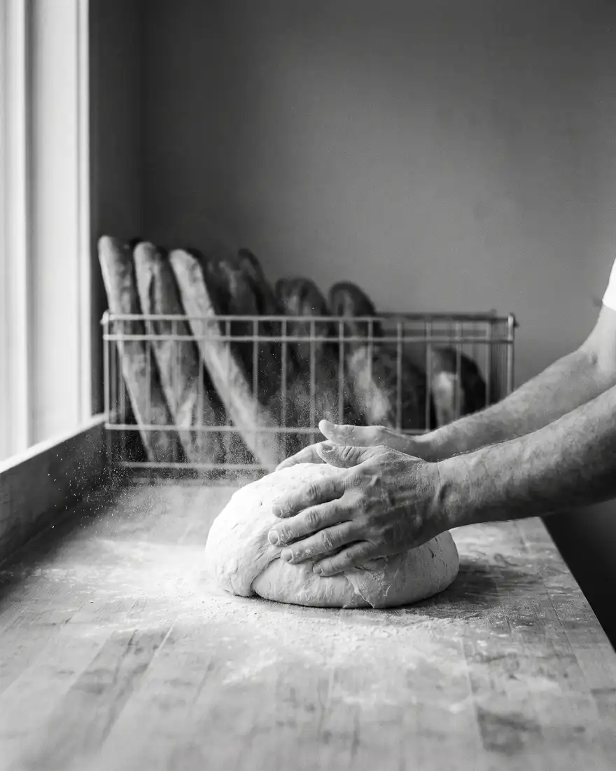 Les mains d’un boulanger façonnant un pâton sur un plan de travail fariné.
