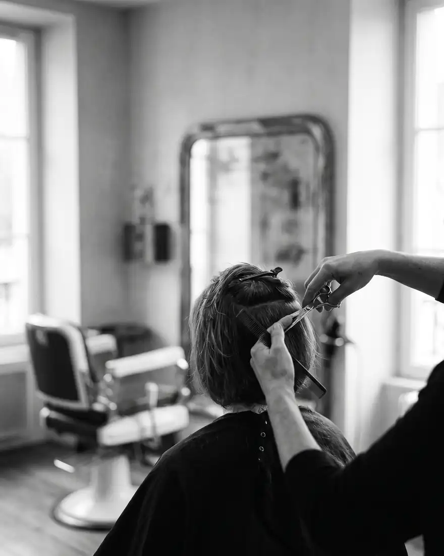 Les mains d’un coiffeur, ciseaux et peigne, pendant une coupe en salon.
